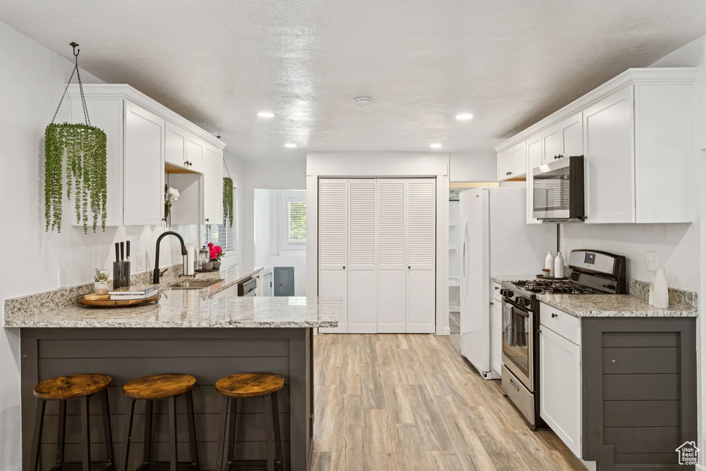 Kitchen featuring stainless steel appliances, light stone counters, light wood finished floors, white cabinetry, and recessed lighting