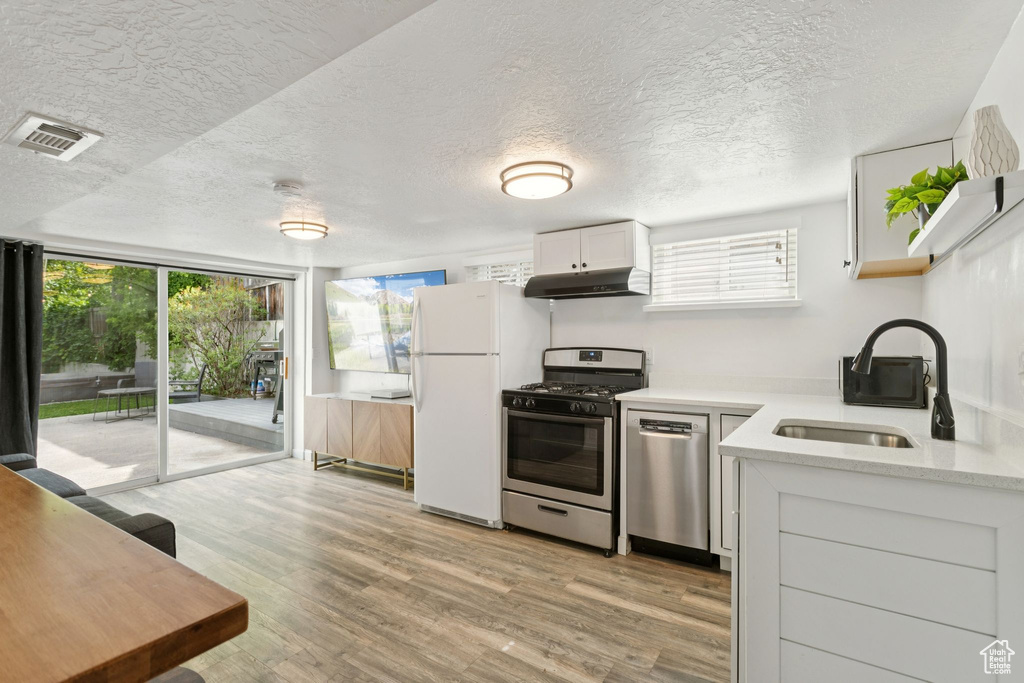 Kitchen with stainless steel appliances, under cabinet range hood, plenty of natural light, a textured ceiling, and light wood finished floors