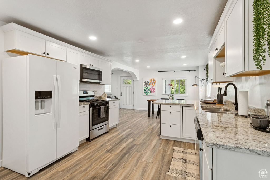 Kitchen featuring stainless steel appliances, arched walkways, light wood finished floors, recessed lighting, and white cabinets