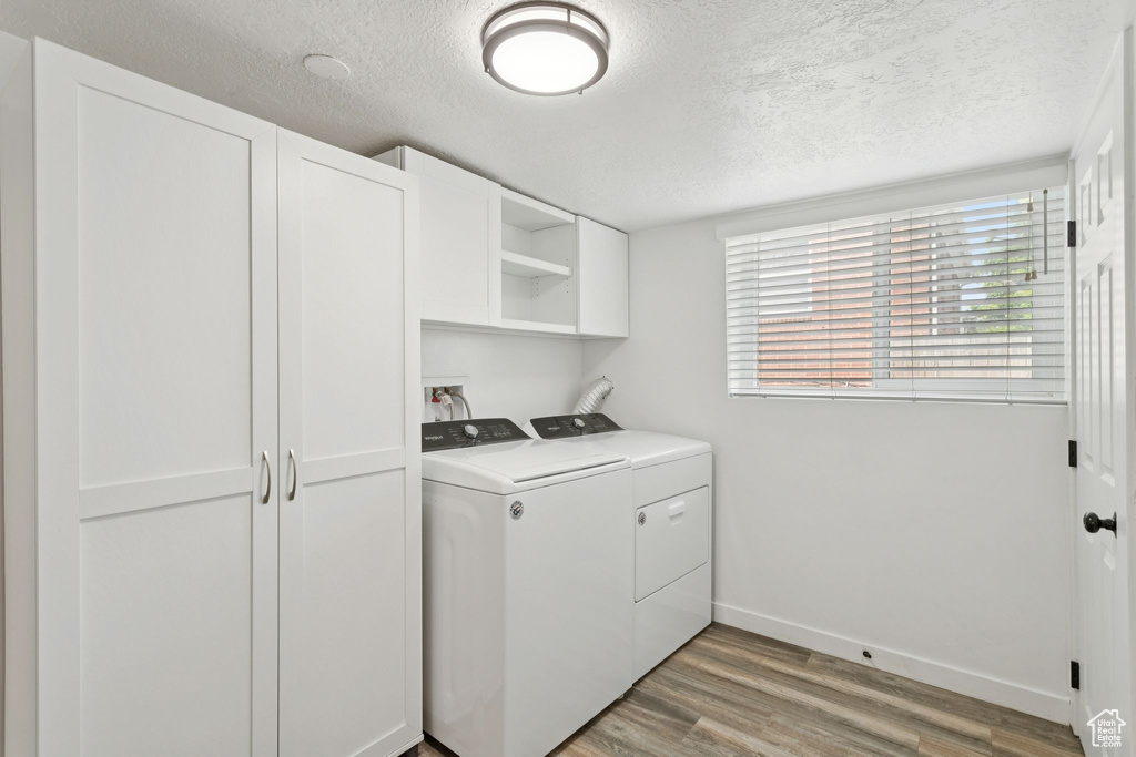 Laundry area with a textured ceiling, washing machine and dryer, and light wood-style flooring