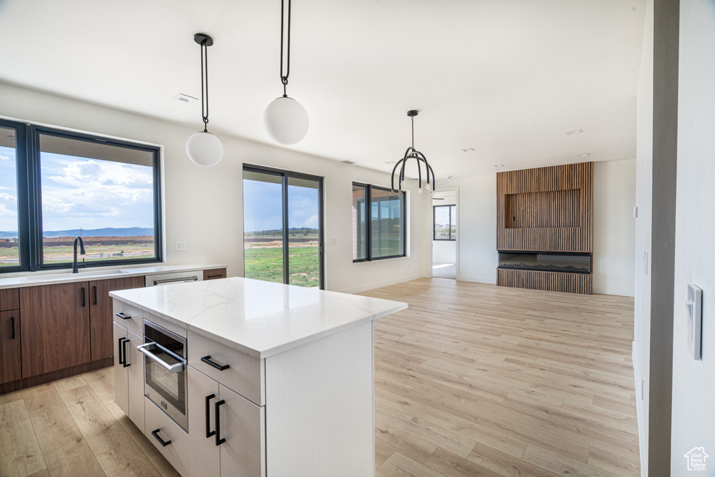 Kitchen with light wood-style floors, a center island, modern cabinets, open floor plan, and hanging light fixtures