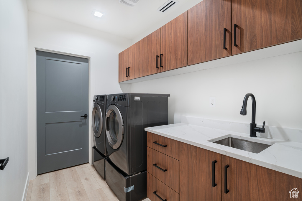 Laundry area featuring washing machine and dryer, cabinet space, and light wood-style flooring