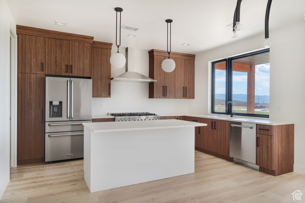 Kitchen featuring appliances with stainless steel finishes, wall chimney range hood, a kitchen island, light countertops, and light wood-style floors