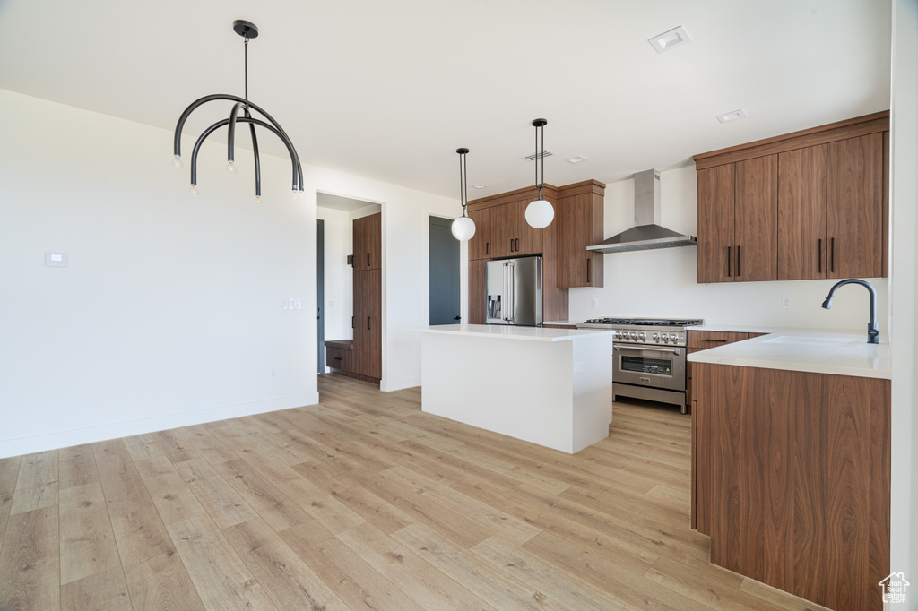 Kitchen with wall chimney range hood, appliances with stainless steel finishes, a center island, and light wood-type flooring