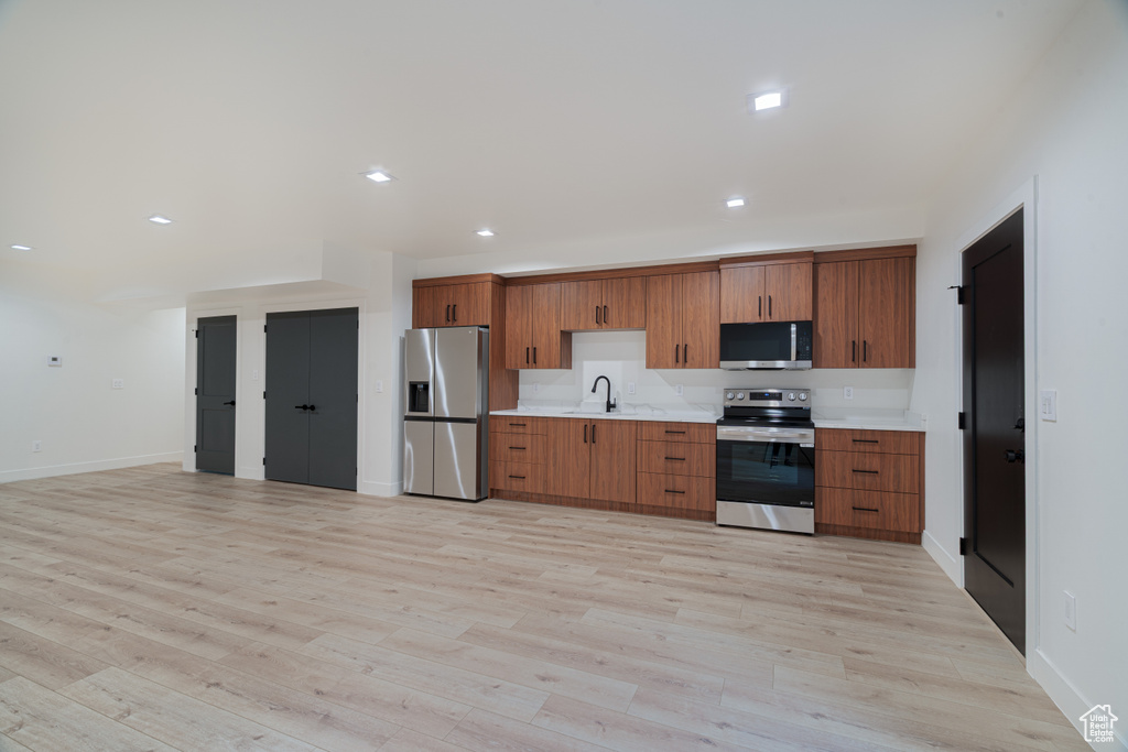 Kitchen featuring appliances with stainless steel finishes, light wood-type flooring, light countertops, brown cabinetry, and recessed lighting
