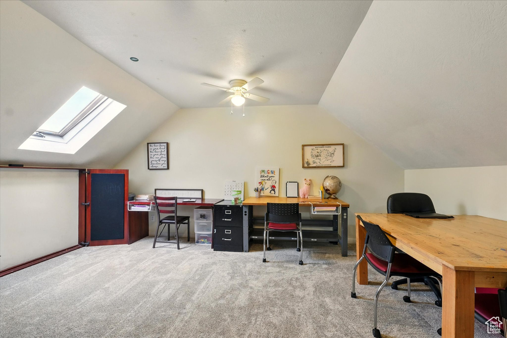 Carpeted office with vaulted ceiling, a skylight, and ceiling fan
