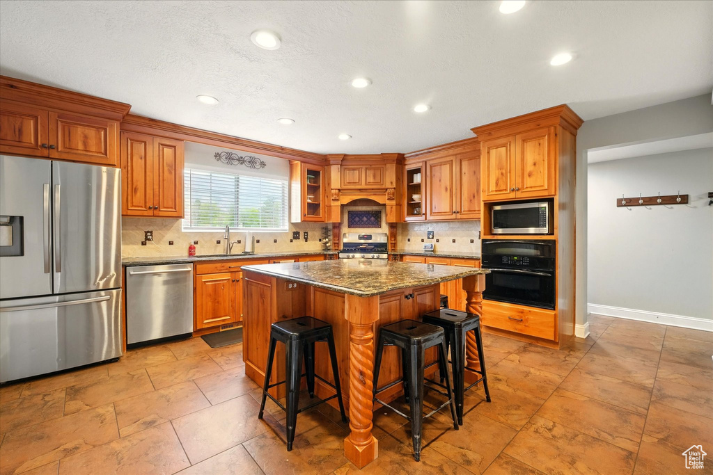 Kitchen featuring stainless steel appliances, brown cabinets, tasteful backsplash, recessed lighting, and a kitchen island