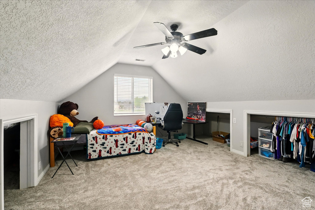 Carpeted bedroom featuring a textured ceiling, vaulted ceiling, and a ceiling fan