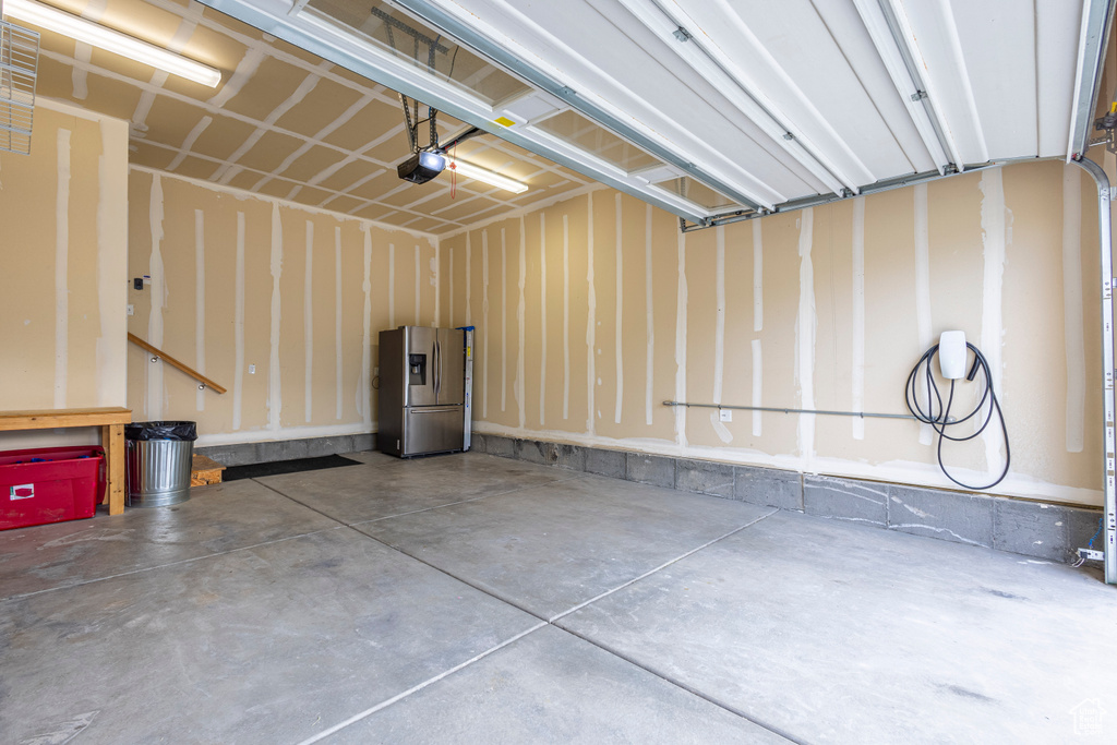 Garage featuring stainless steel fridge with ice dispenser and a garage door opener