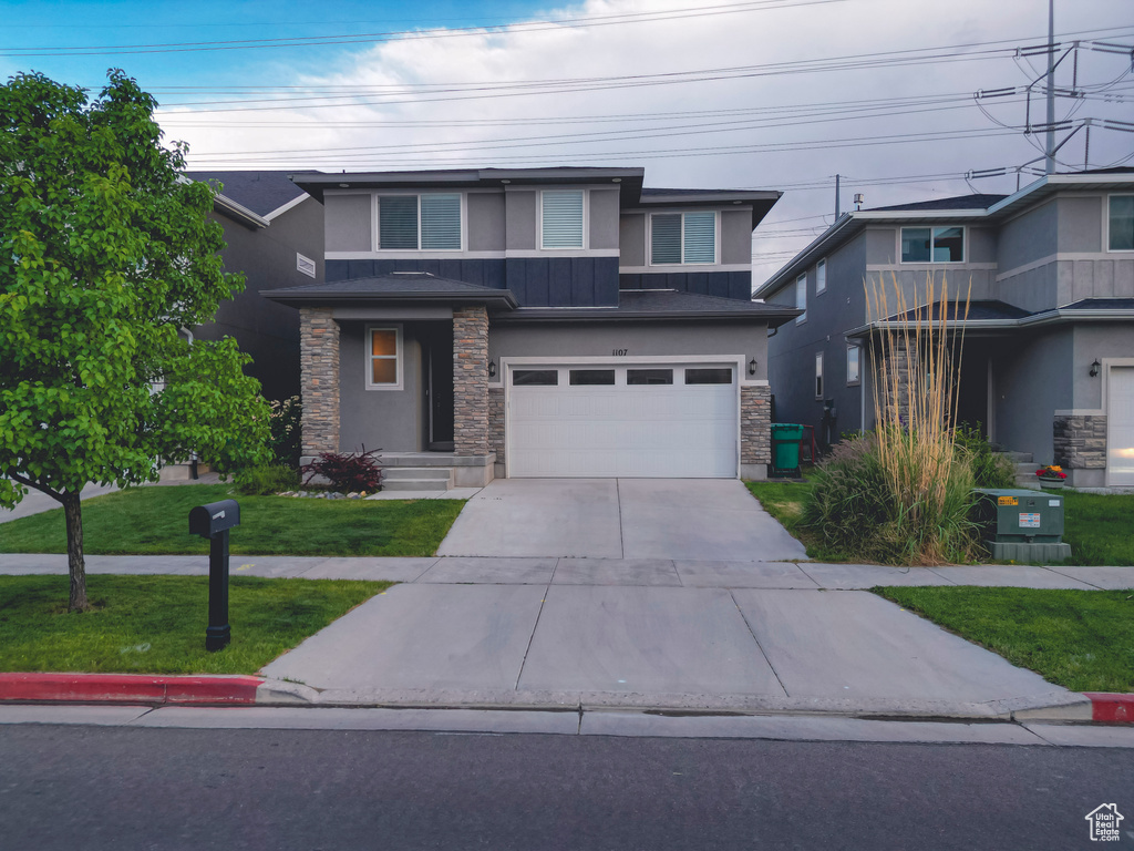 Prairie-style home featuring stone siding, stucco siding, a garage, concrete driveway, and a front lawn