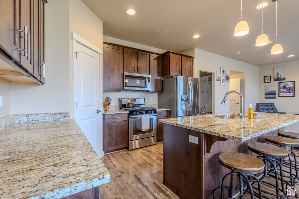 Kitchen featuring stainless steel appliances, light wood-style flooring, a kitchen breakfast bar, light stone counters, and hanging light fixtures