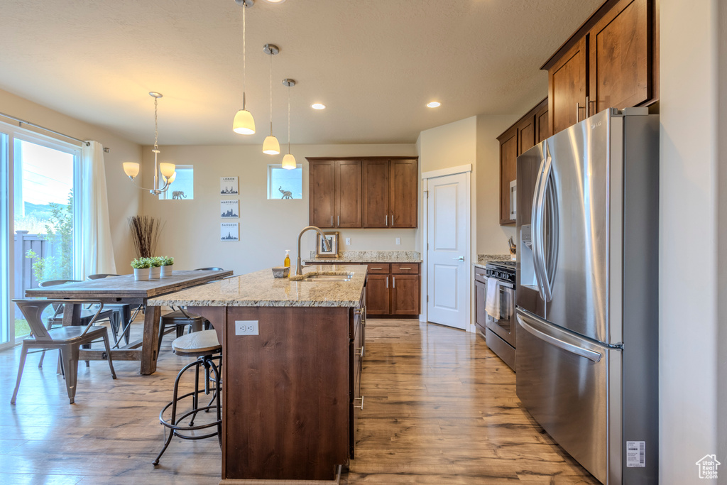 Kitchen with appliances with stainless steel finishes, light wood finished floors, a breakfast bar area, an island with sink, and recessed lighting