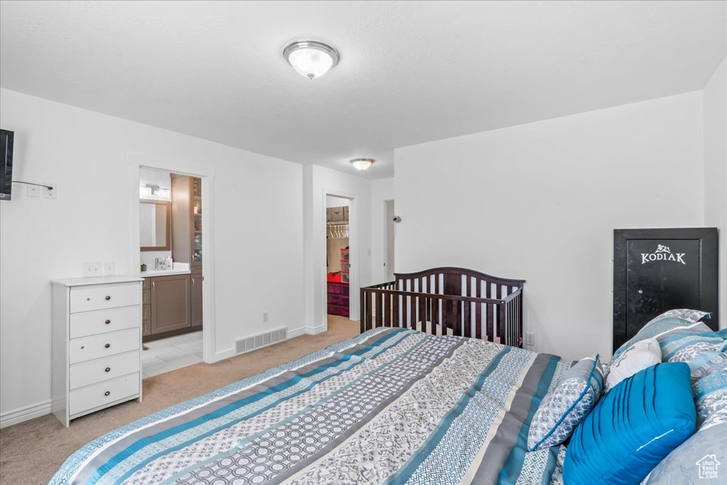 Bedroom featuring light carpet, a walk in closet, and ensuite bath