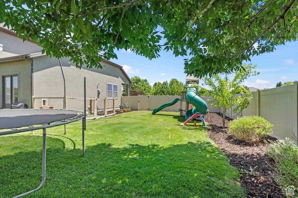 Fenced backyard featuring a playground and a trampoline