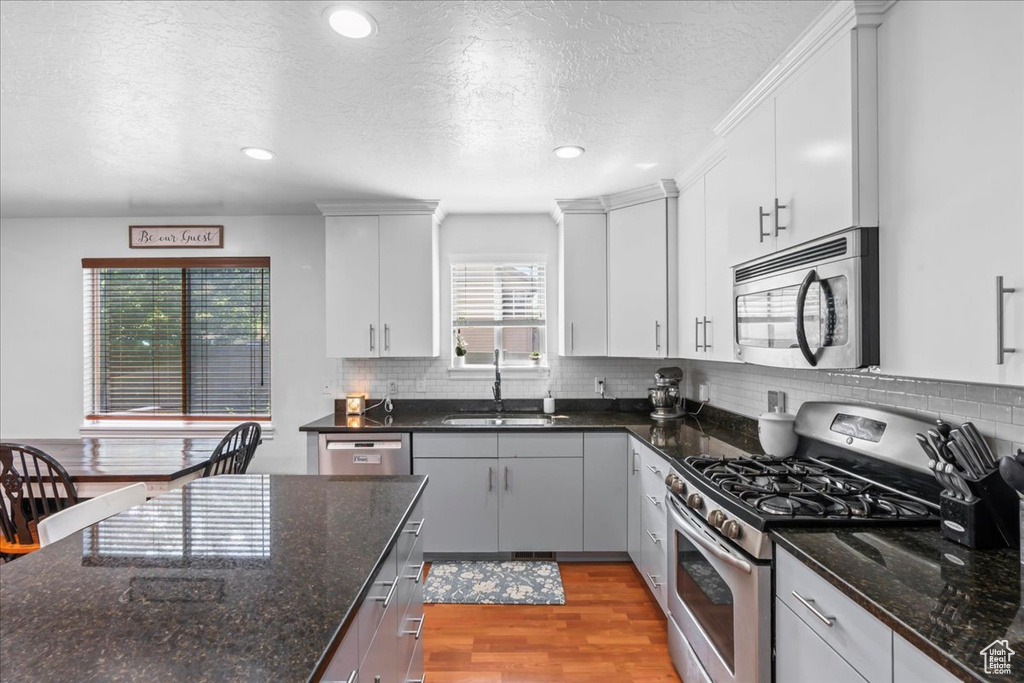 Kitchen with stainless steel appliances, light wood-style floors, a textured ceiling, white cabinets, and tasteful backsplash