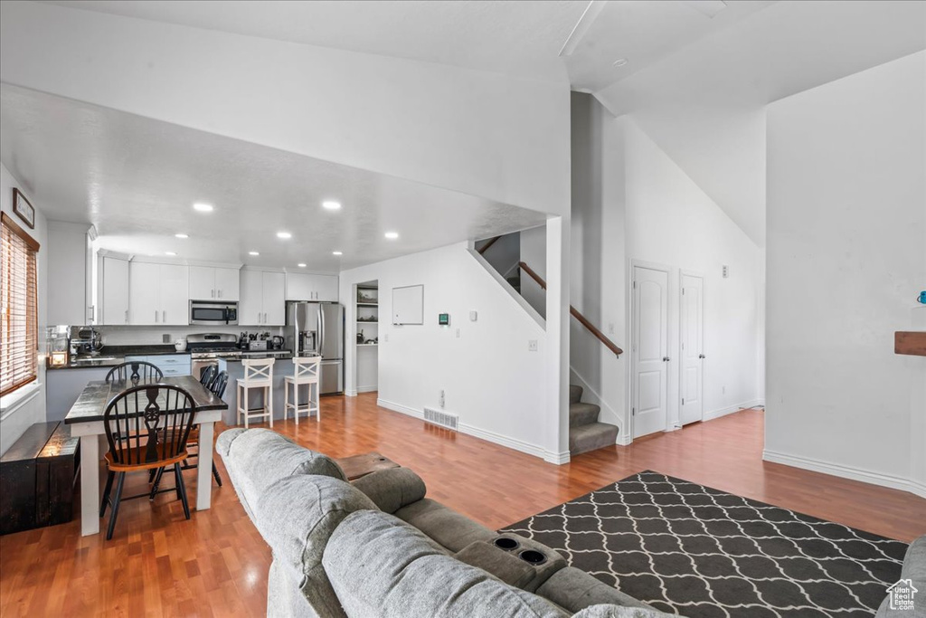 Living room featuring light wood-style floors, stairway, recessed lighting, and high vaulted ceiling