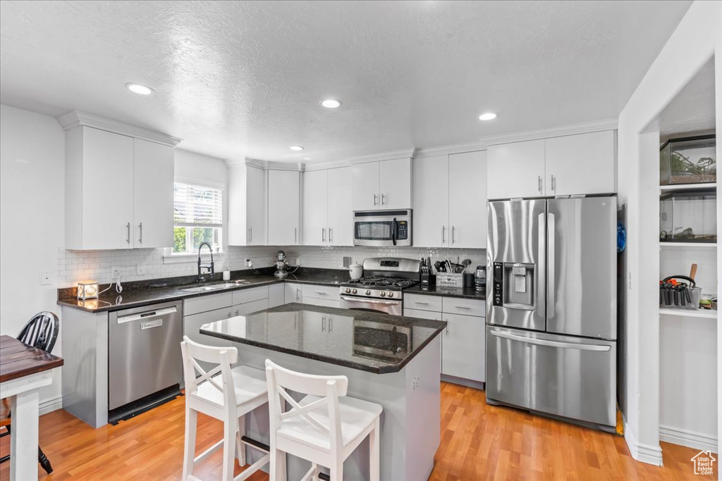 Kitchen featuring appliances with stainless steel finishes, light wood-type flooring, tasteful backsplash, a kitchen island, and a kitchen bar