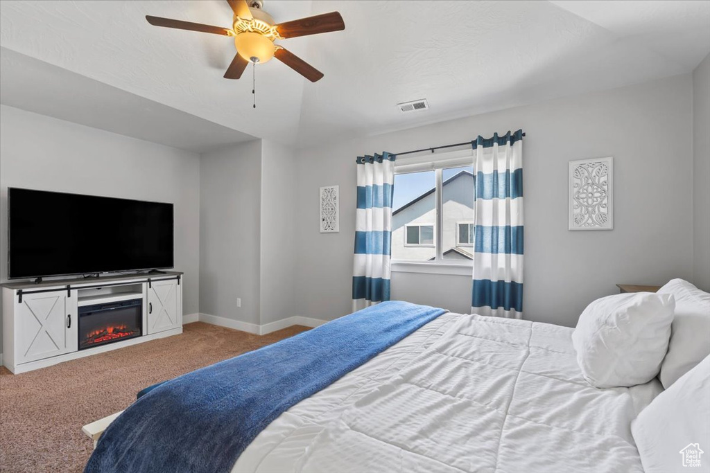 Bedroom with carpet, a ceiling fan, and a glass covered fireplace