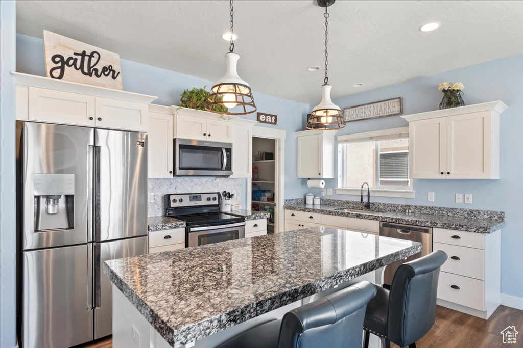 Kitchen with appliances with stainless steel finishes, dark wood-style floors, a breakfast bar, a kitchen island, and white cabinetry