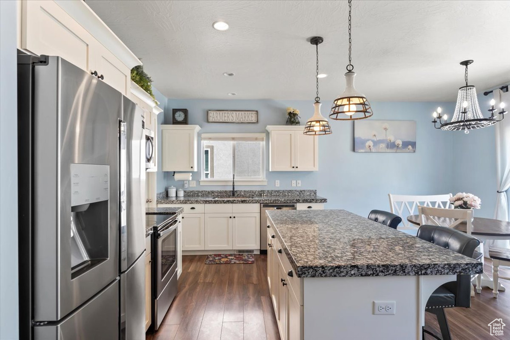 Kitchen with appliances with stainless steel finishes, dark wood-style flooring, a breakfast bar, dark countertops, and a kitchen island