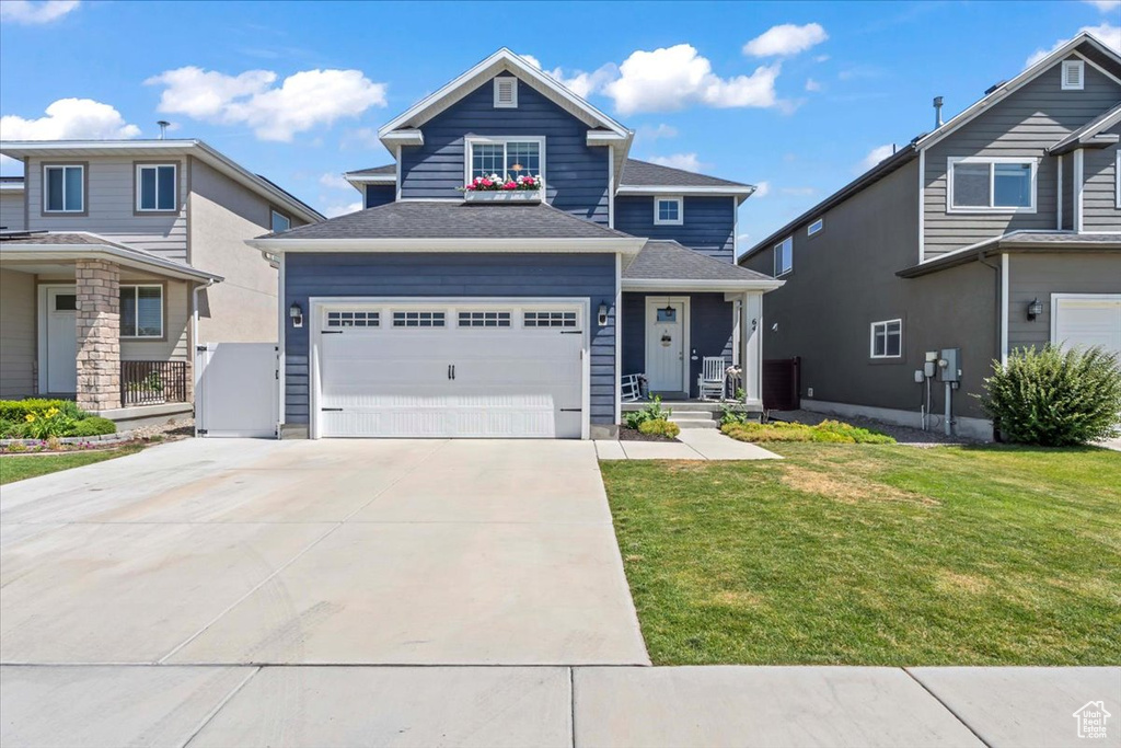 View of front facade with a front yard, concrete driveway, an attached garage, and a shingled roof