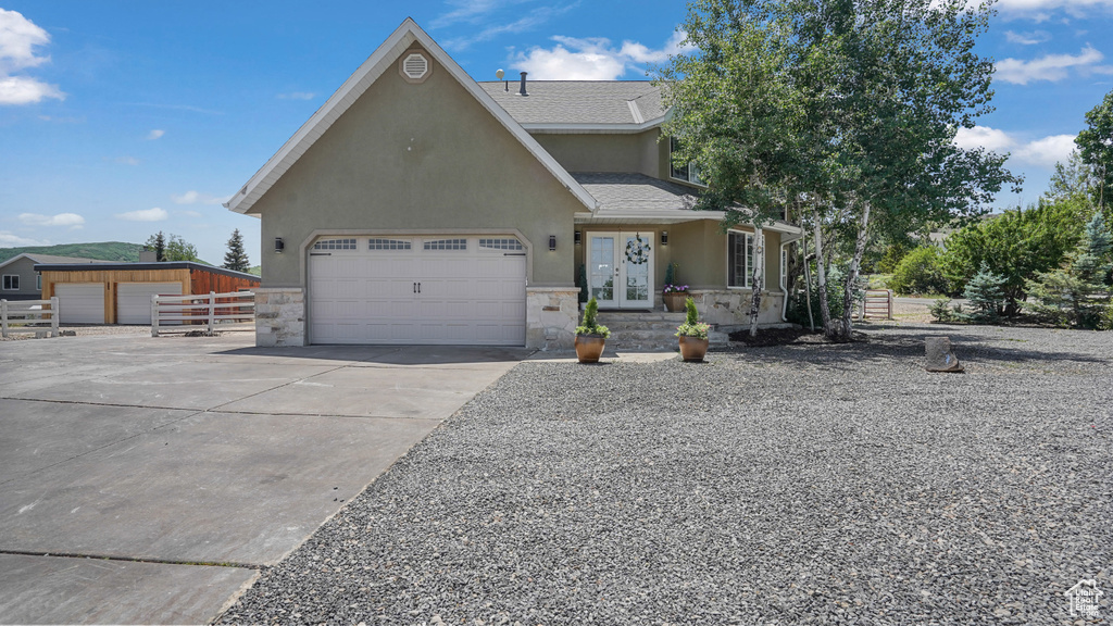 View of front facade with stucco siding, stone siding, driveway, a garage, and french doors