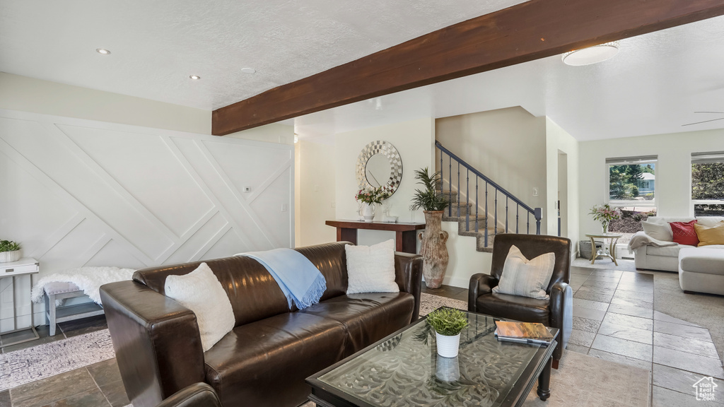 Living room featuring stairs, beamed ceiling, stone tile floors, and recessed lighting