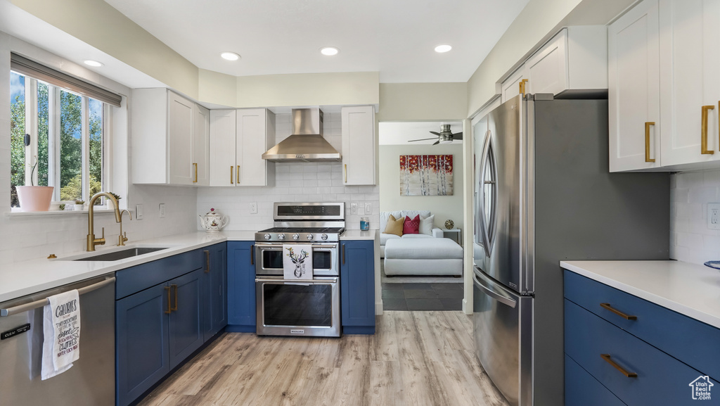 Kitchen featuring stainless steel appliances, wall chimney range hood, blue cabinets, white cabinetry, and recessed lighting