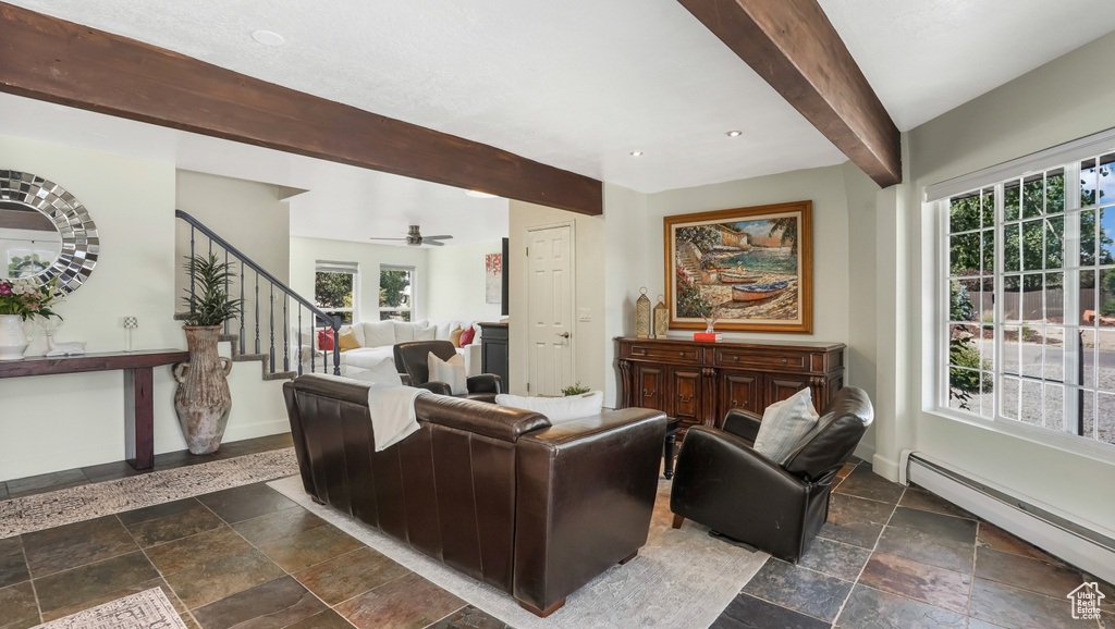 Living area featuring a baseboard radiator, stone tile floors, beamed ceiling, stairway, and ceiling fan
