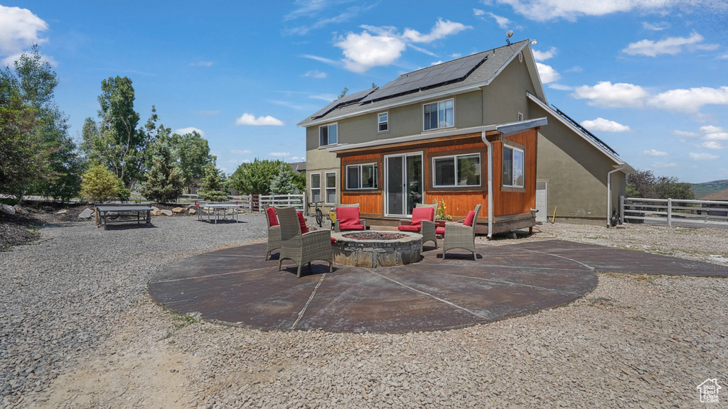 Back of house with an outdoor fire pit, roof mounted solar panels, and a patio area