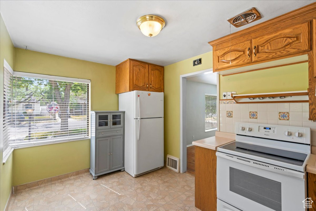Kitchen featuring white appliances, tasteful backsplash, light countertops, and brown cabinetry