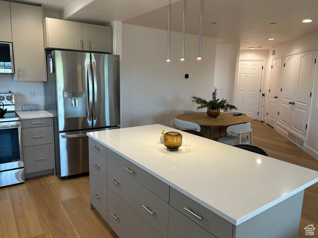 Kitchen featuring stainless steel appliances, gray cabinets, light wood-style flooring, light countertops, and a kitchen island