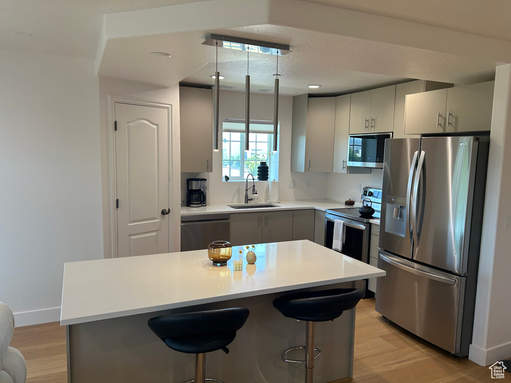 Kitchen with stainless steel appliances, light wood-type flooring, a kitchen bar, light countertops, and a center island