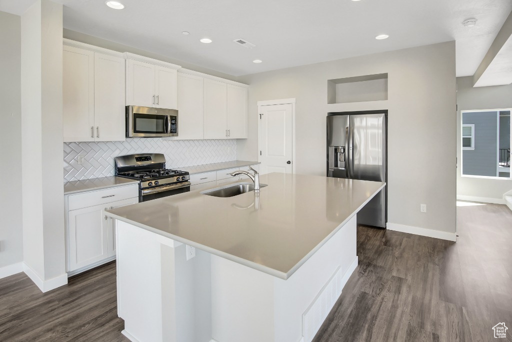 Kitchen with appliances with stainless steel finishes, a center island with sink, dark wood-style floors, backsplash, and white cabinetry