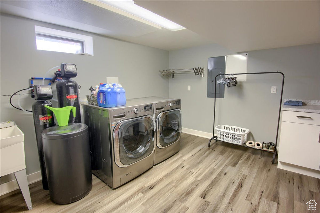 Washroom featuring washing machine and clothes dryer, light wood-style flooring, and electric panel