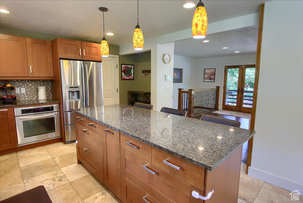 Kitchen featuring appliances with stainless steel finishes, backsplash, brown cabinetry, dark stone counters, and recessed lighting