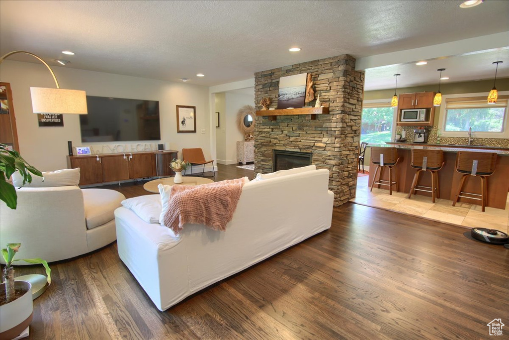 Living area with dark wood-type flooring, recessed lighting, a stone fireplace, and a textured ceiling