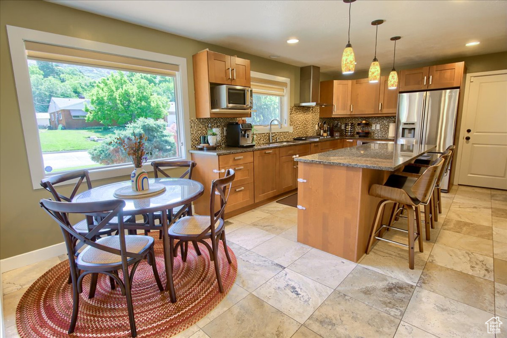 Kitchen with wall chimney exhaust hood, appliances with stainless steel finishes, decorative backsplash, a kitchen island, and dark stone countertops