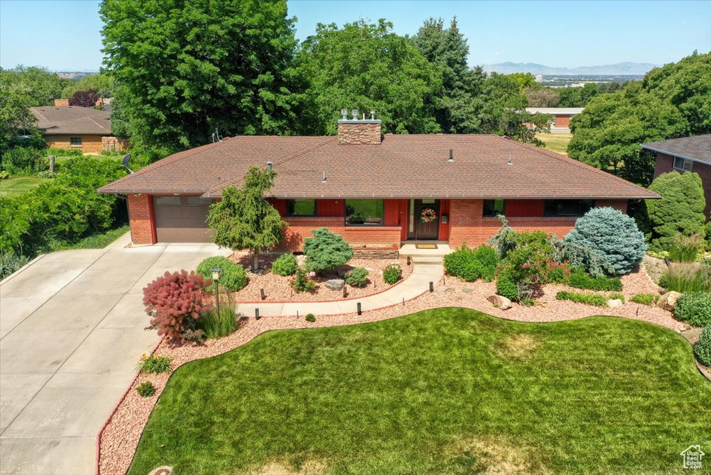 Single story home featuring concrete driveway, a garage, a chimney, brick siding, and a front yard