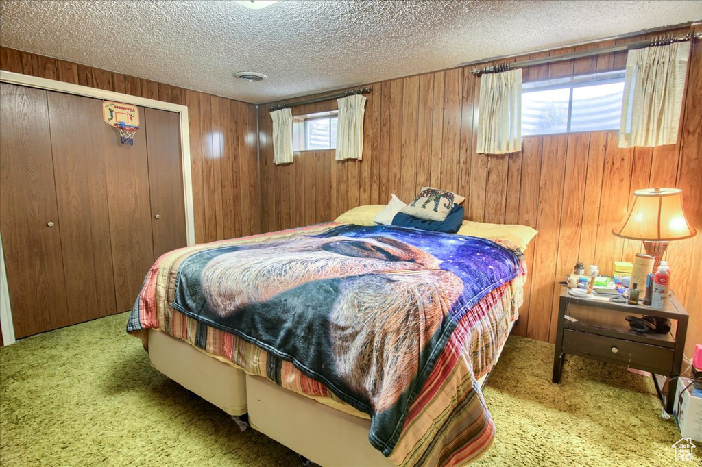 Bedroom featuring carpet, a textured ceiling, wood walls, and a closet
