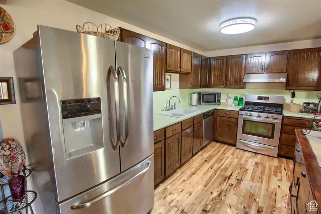 Kitchen featuring appliances with stainless steel finishes, under cabinet range hood, light wood-type flooring, and light countertops