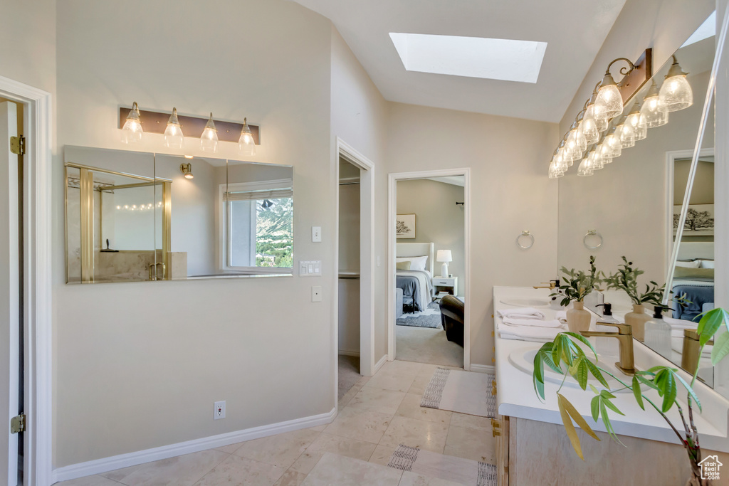 Bathroom featuring a skylight, connected bathroom, double vanity, lofted ceiling, and a shower