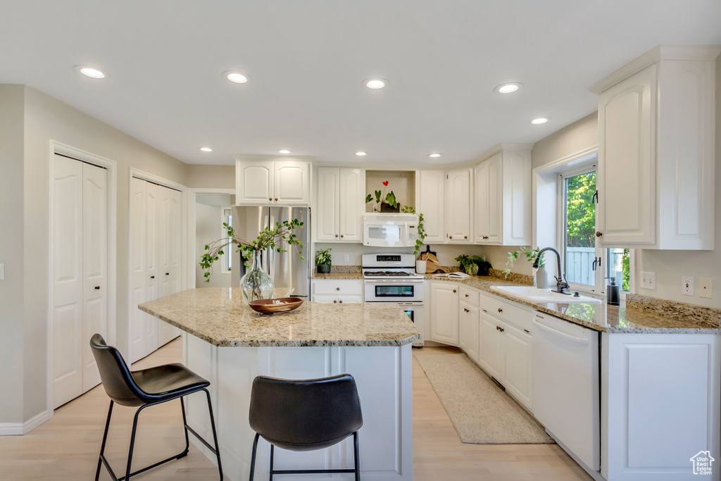 Kitchen with white appliances, a breakfast bar, light wood finished floors, light stone countertops, and recessed lighting