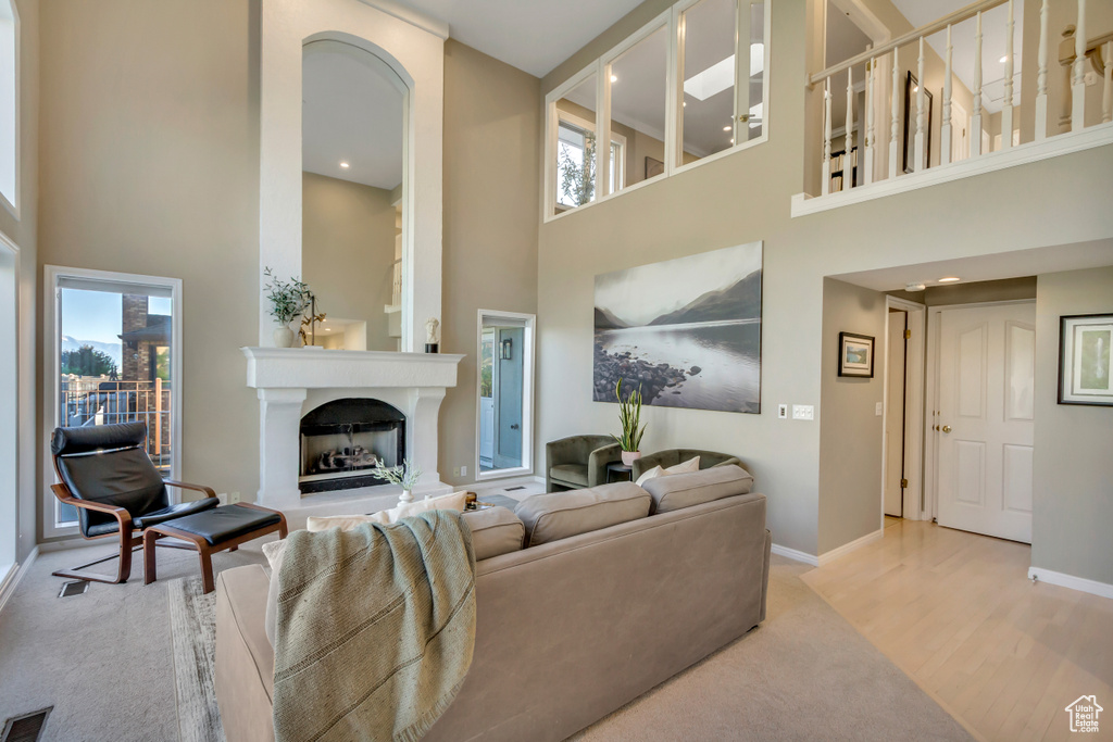 Carpeted living room featuring a towering ceiling, a fireplace with raised hearth, healthy amount of natural light, and recessed lighting
