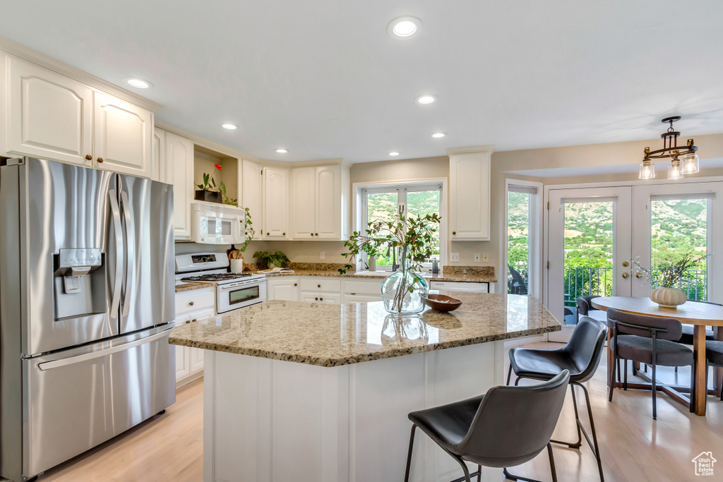 Kitchen with white appliances, french doors, light stone counters, light wood-style floors, and a kitchen breakfast bar