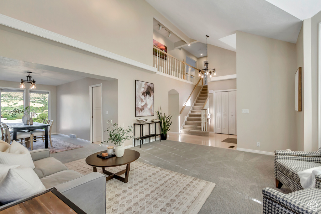 Carpeted living area featuring a chandelier, high vaulted ceiling, stairway, and arched walkways