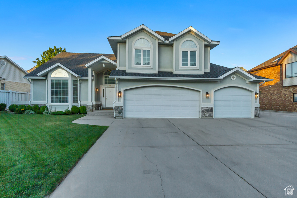 View of front of property with stucco siding, driveway, a front yard, and stone siding