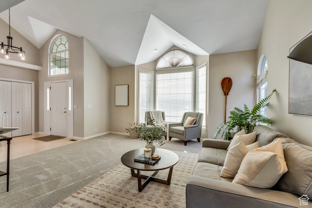 Living area with a chandelier, light carpet, plenty of natural light, and high vaulted ceiling