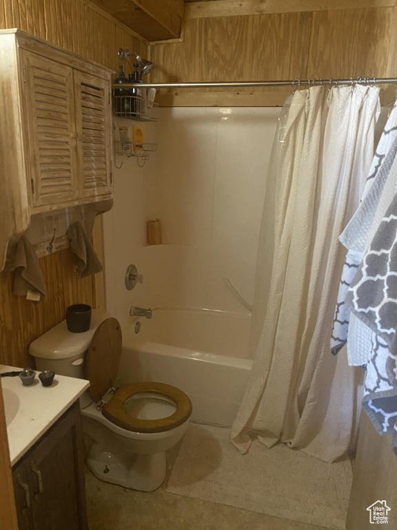 Full bath featuring vanity, wooden walls, shower / bath combo with shower curtain, and tile patterned flooring
