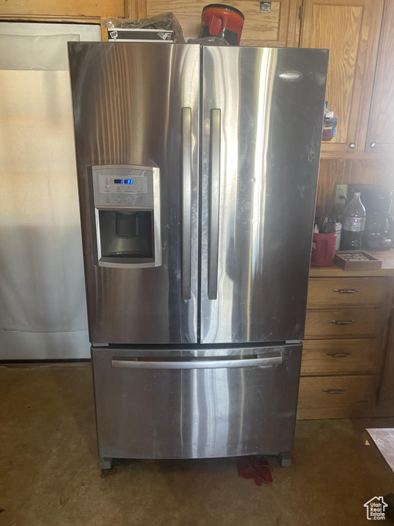 Kitchen featuring stainless steel refrigerator with ice dispenser, brown cabinets, and concrete floors